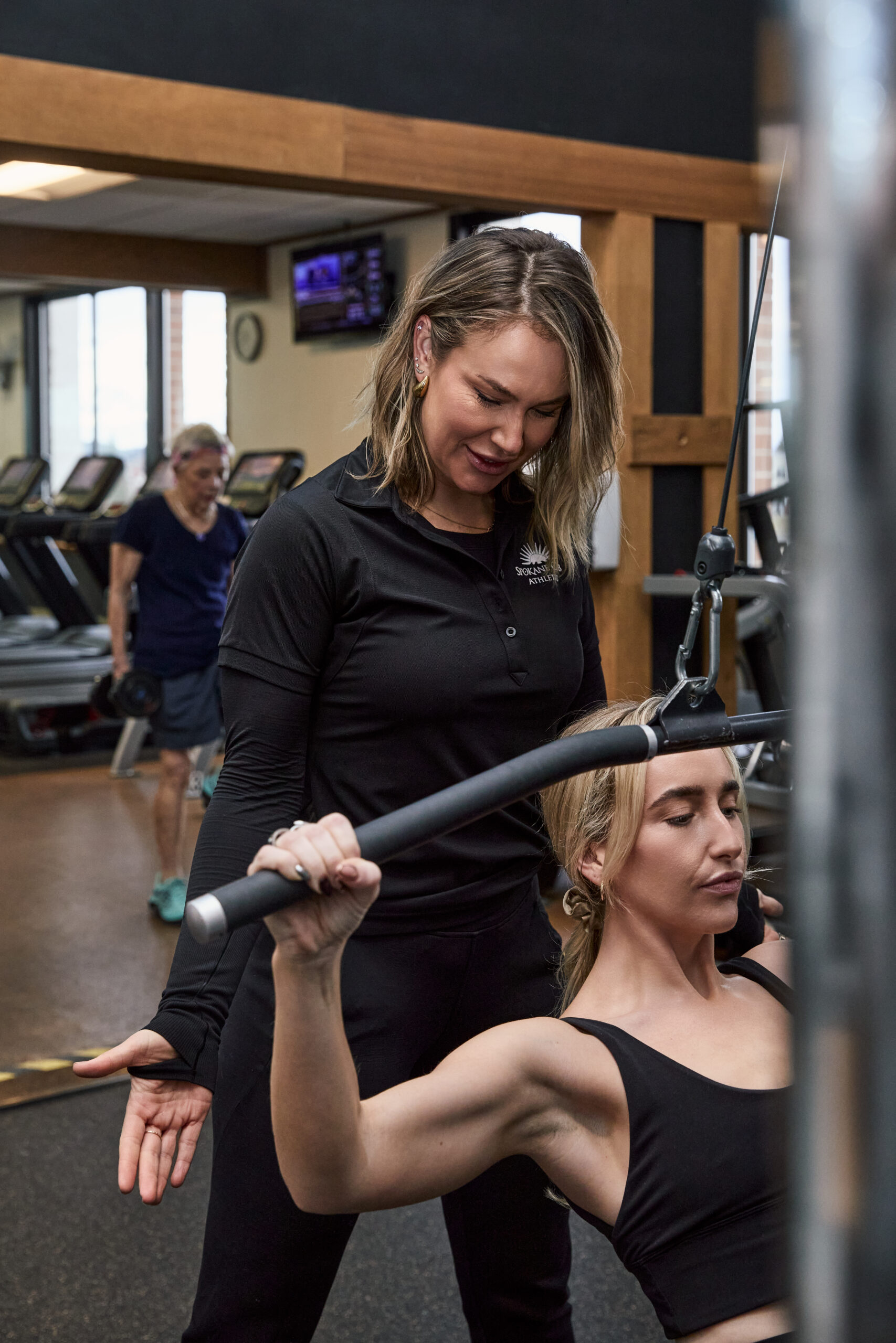 6Y4A6031 Personal trainer assisting woman doing pulldown exercises